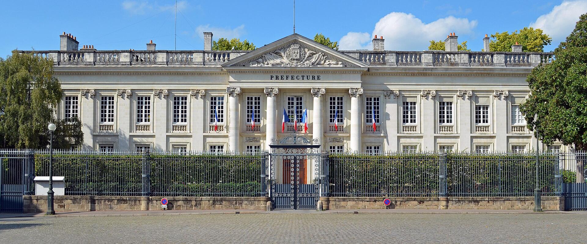 1. A grand neoclassical building with a pediment, columns, and the word "PREFECTURE" inscribed above the entrance, fronted by a wrought-iron fence and cobblestone plaza under a blue sky.