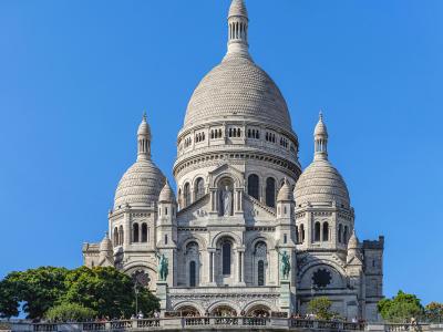 Frontal view of the white-domed Basilica of Sacré-Cœur in Montmartre, Paris, under a clear blue sky.
