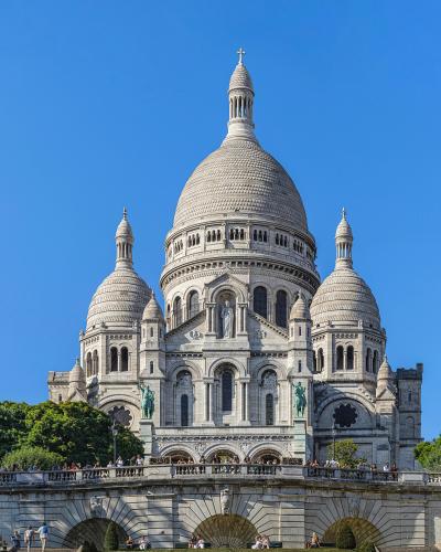Frontal view of the white-domed Basilica of Sacré-Cœur in Montmartre, Paris, under a clear blue sky.