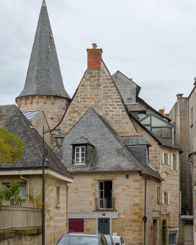 A street scene showing historic stone buildings with slate roofs, including a prominent conical turret, and parked cars along the road.