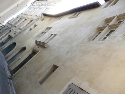 A low-angle, tilted photograph of the beige stucco facade of a historic building featuring arched windows and stone window surrounds.