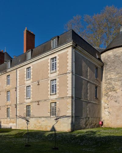 A large, multi-story stone and stucco building with a prominent round stone tower, red brick chimneys, and modern wire sculptures in the foreground, identified as the Château de Tours (specifically the Musée des Beaux-Arts de Tours).