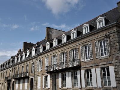 A row of historic stone townhouses with mansard roofs, dormer windows, and white shutters under a blue sky.