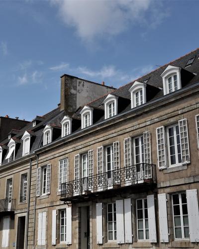 A row of historic stone townhouses with mansard roofs, dormer windows, and white shutters under a blue sky.