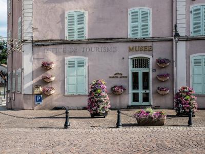 A pink building facade with light blue shutters, displaying signage for "OFFICE DE TOURISME" and "MUSEE MARIUS AUDIN," adorned with flower baskets and situated on a cobblestone street.