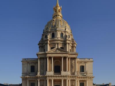 An interior view of a grand stone staircase with ornate black iron railings, tall arched windows, and a vaulted ceiling with faded frescoes, identified by the filename as the "Escaliers Est" (East Stairs) of Les Invalides.