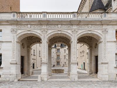 The image shows the ornate stone arcade of the Cour d'Honneur (Courtyard of Honor) at the Château de Pau, featuring three large arches with intricate Renaissance carvings and royal monograms, leading into an inner courtyard with a fountain.