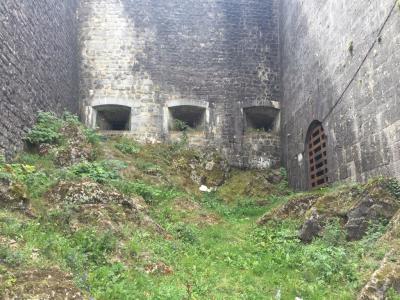 A view of the interior of a stone fortification featuring three arched gun ports on the back wall and a barred arched doorway on the right, with a grassy, rocky slope in the foreground.