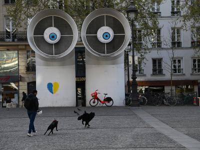 Two large, eye-covered ventilation towers at Place Georges Pompidou in Paris with pedestrians and dogs.