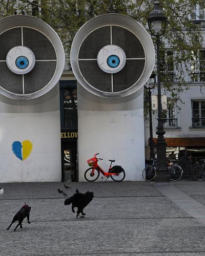 Two large, eye-covered ventilation towers at Place Georges Pompidou in Paris with pedestrians and dogs.