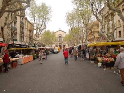 A wide tree-lined avenue in Toulon filled with market stalls and pedestrians leading to a church.