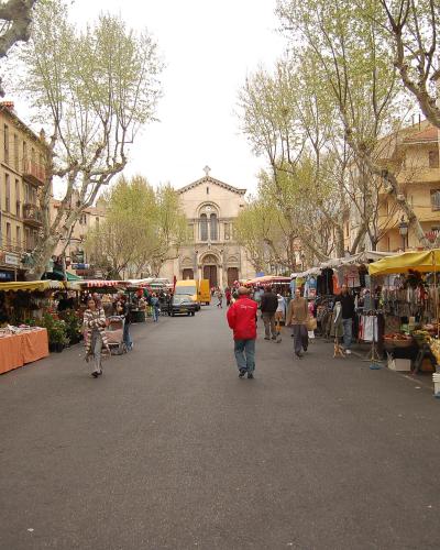A wide tree-lined avenue in Toulon filled with market stalls and pedestrians leading to a church.