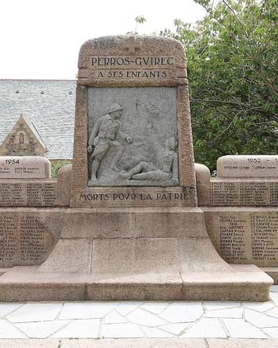 A stone war memorial featuring a central relief sculpture and inscribed lists of names, situated on a paved area with a stone church visible in the background.