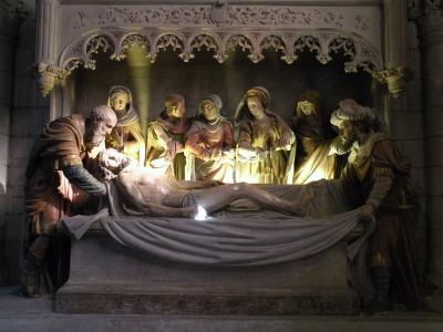 The image shows a detailed sculptural group depicting the Lamentation or Entombment of Christ, featuring multiple figures in Renaissance-style robes gathered around a recumbent body on a stone slab, set within an ornate Gothic architectural niche