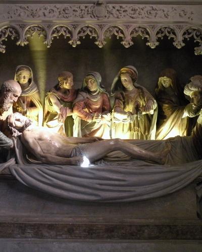 The image shows a detailed sculptural group depicting the Lamentation or Entombment of Christ, featuring multiple figures in Renaissance-style robes gathered around a recumbent body on a stone slab, set within an ornate Gothic architectural niche