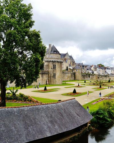 A view of the Jardin des Remparts (Walls Garden) in Vannes, France, featuring manicured lawns, flowerbeds, a canal, and the historic stone ramparts with the Tour de la Reine and the Palais Rohan in the background.