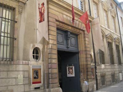The image shows the exterior entrance of a stone building with signage reading "MUSEE MAGNIN" above the door and banners displaying "MAGNIN," located on a paved street.