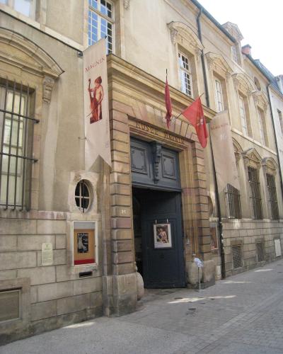 The image shows the exterior entrance of a stone building with signage reading "MUSEE MAGNIN" above the door and banners displaying "MAGNIN," located on a paved street.