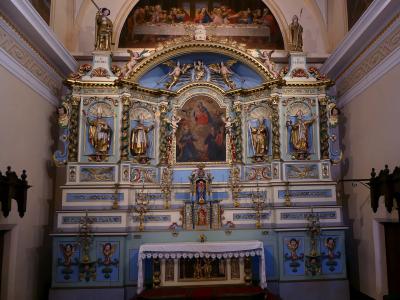 An ornate, light-blue and gold altarpiece (retable) inside a church, featuring statues of saints, a central painting of the Last Supper, and inscriptions reading "S. MICHEL" and "S. CLAUDE".