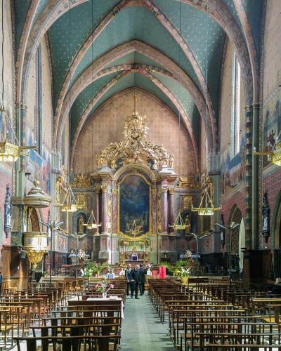 The image shows the interior nave and chancel of a large Gothic church with distinctive blue vaulted ceilings decorated with gold stars, painted murals on the walls, and an ornate golden altarpiece.