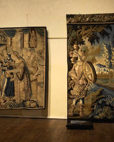 Two large, historic tapestries displayed on a museum wall with wooden flooring and informational plaques beneath them.