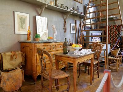 One line: The interior of a historic artist's studio featuring wooden furniture, a ladder, shelves with pottery, and a rope barrier indicating it is a preserved museum space.