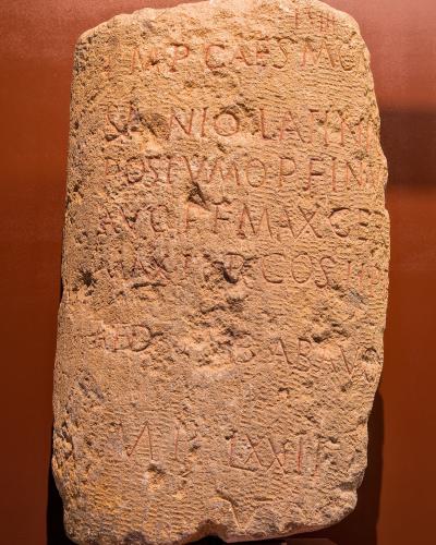 A Roman milestone with Latin inscriptions displayed on a museum pedestal.