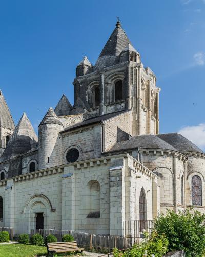 The image shows the exterior of a large Romanesque stone church with multiple conical slate roofs, towers, and an apse, set against a blue sky with green landscaping in the foreground.