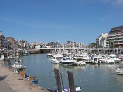 Sunlit French harbor filled with pleasure boats and boats, framed by quayside buildings and a bridge under a clear blue sky.