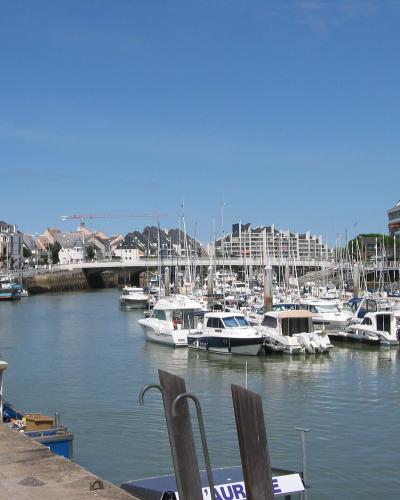 Sunlit French harbor filled with pleasure boats and boats, framed by quayside buildings and a bridge under a clear blue sky.