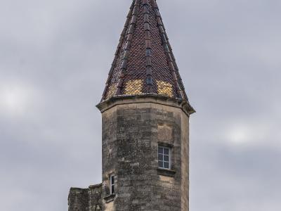 A stone tower with a conical tiled roof and a weather vane, part of a larger fortified stone structure.