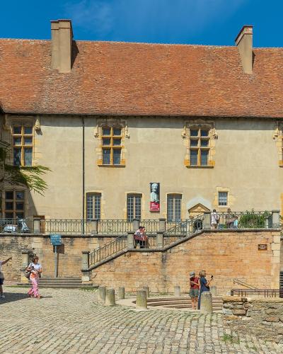 The Abbey Palace in Cluny, Burgundy, with tourists on a cobblestone forecourt.