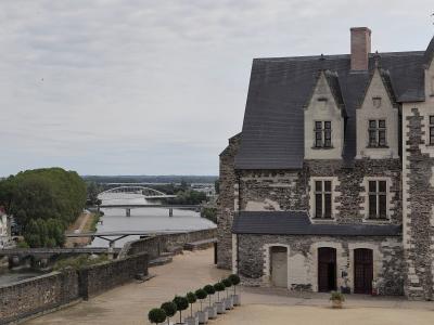 The image shows the stone facade and slate roof of the Royal Lodge (Logis Royal) at Château d'Angers, with the Maine River, the Pont d'Angers, and the modern Pont de l'Europe visible in the background.