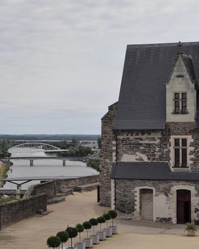 The image shows the stone facade and slate roof of the Royal Lodge (Logis Royal) at Château d'Angers, with the Maine River, the Pont d'Angers, and the modern Pont de l'Europe visible in the background.