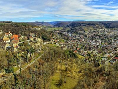 A panoramic landscape view of a town nestled in a river valley with a prominent cluster of historic buildings perched on a rocky cliff overlooking the settlement below.