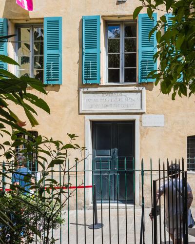 Maison Bonaparte in Ajaccio, Corsica, featuring its iconic yellow facade, blue shutters, and commemorative stone plaque above the entrance.