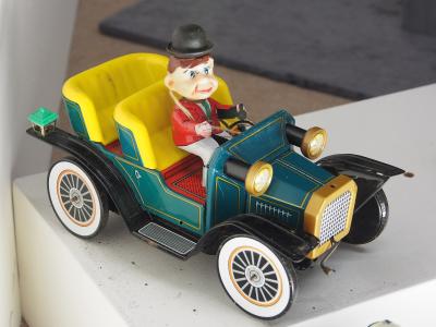 A vintage tin lithograph toy car with a wind-up driver figure, displayed on a white surface indoors.