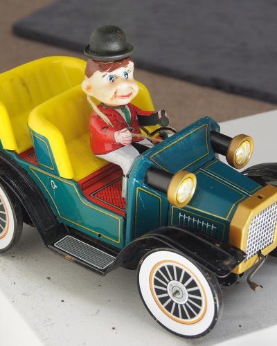 A vintage tin lithograph toy car with a wind-up driver figure, displayed on a white surface indoors.