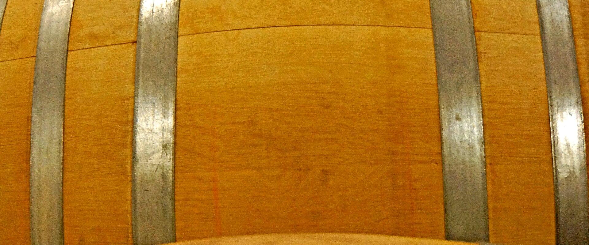 A close-up view of several large wooden wine barrels with metal hoops, stacked in a dimly lit cellar or aging room.