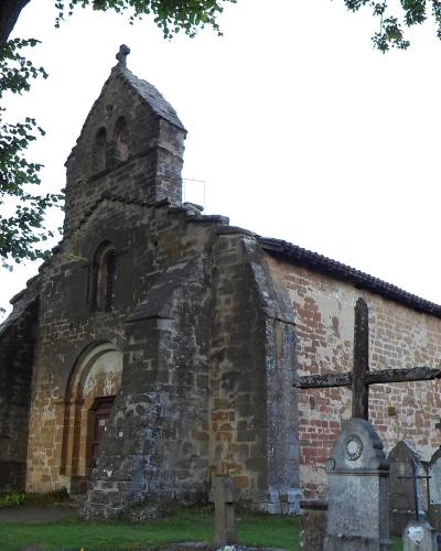 A stone chapel with a bell gable stands within a graveyard under a large tree.