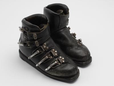 A pair of vintage black leather ski boots with metal buckles and straps, photographed against a plain white background.