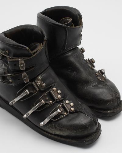 A pair of vintage black leather ski boots with metal buckles and straps, photographed against a plain white background.