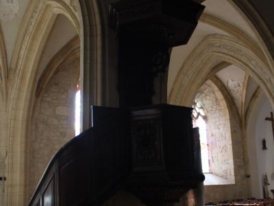 The image shows the interior of a church featuring a prominent, dark wooden pulpit with a curved staircase, set against stone walls and Gothic-style vaulted arches.