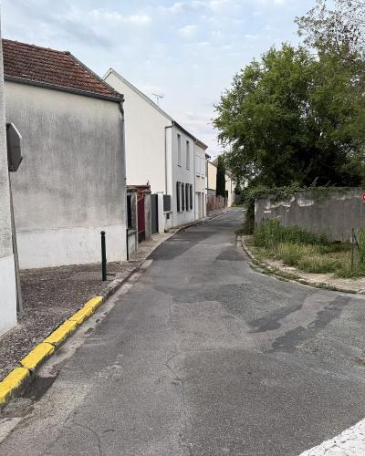 A narrow paved street in a French town with a blue street sign on the left wall reading "RUE DES REMPARTS" and a matching sign on a pole to the right, alongside a "No Entry" traffic sign and a concrete wall bordering a green area.