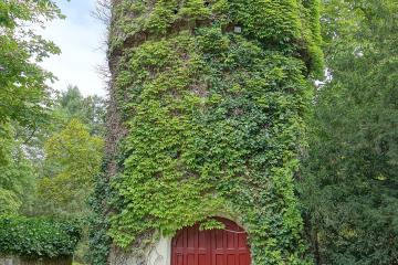 1. A tall, cylindrical stone tower heavily covered in green ivy with a red wooden door at its base, situated in a grassy garden area.