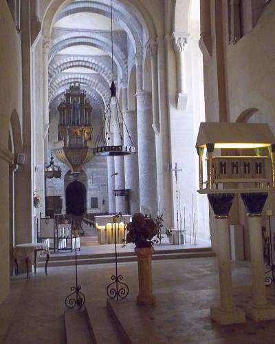 The interior nave of a Romanesque church featuring a barrel-vaulted ceiling, massive cylindrical columns, a large pipe organ at the far end, and a wooden lectern in the foreground.