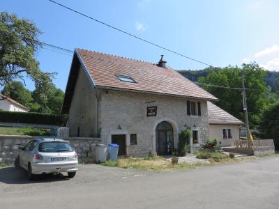 A stone farmhouse with a tiled roof and a hanging sign reading "FERME AUBERGE LA BERGERIE", with a silver car parked in front.
