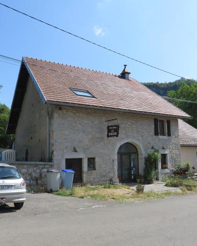 A stone farmhouse with a tiled roof and a hanging sign reading "FERME AUBERGE LA BERGERIE", with a silver car parked in front.