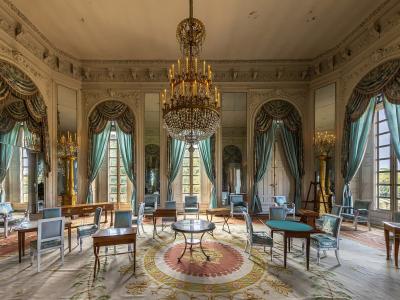 An interior view of a grand, octagonal salon featuring a large crystal chandelier, mirrored walls, teal drapery, and period furniture.