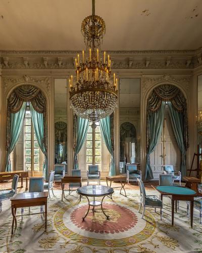An interior view of a grand, octagonal salon featuring a large crystal chandelier, mirrored walls, teal drapery, and period furniture.